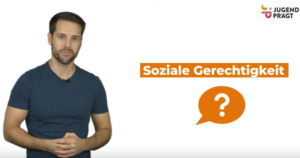 Zu sehen ist ein Ausschnitt des Videos Was ist soziale Gerechtigkeit?. Dort steht ein Mann mit kurzen braunen Haaren, er hat ein blaues T-Shirt und die Hände verschränkt. Daneben steht "Soziale Gerechtigkeit?".